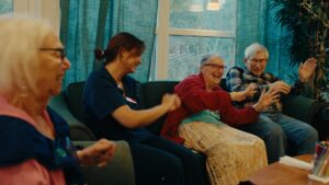 Flera äldre på ett äldreboende som dansar tillsammans i soffan